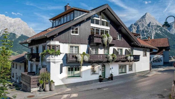 Een traditioneel hotel in chalethuis-stijl met een steile dakschild, grote ramen en balkons met hangende planten.