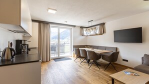 Een moderne keuken met een koffiezetapparaat, een eethoek met tafel en stoelen, een bank en een aan de muur bevestigde televisie.