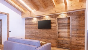 Quarto moderno com paredes de madeira, televisão de tela plana e sofá cinza.