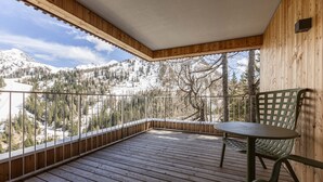 Una terraza de madera con una mesa y sillas, con vista a un paisaje montañoso nevado.