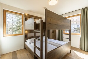 Ein Schlafraum mit Etagenbetten, einem Holz-Kopfteil, großen Fenstern und Blick auf ein Gebäude.