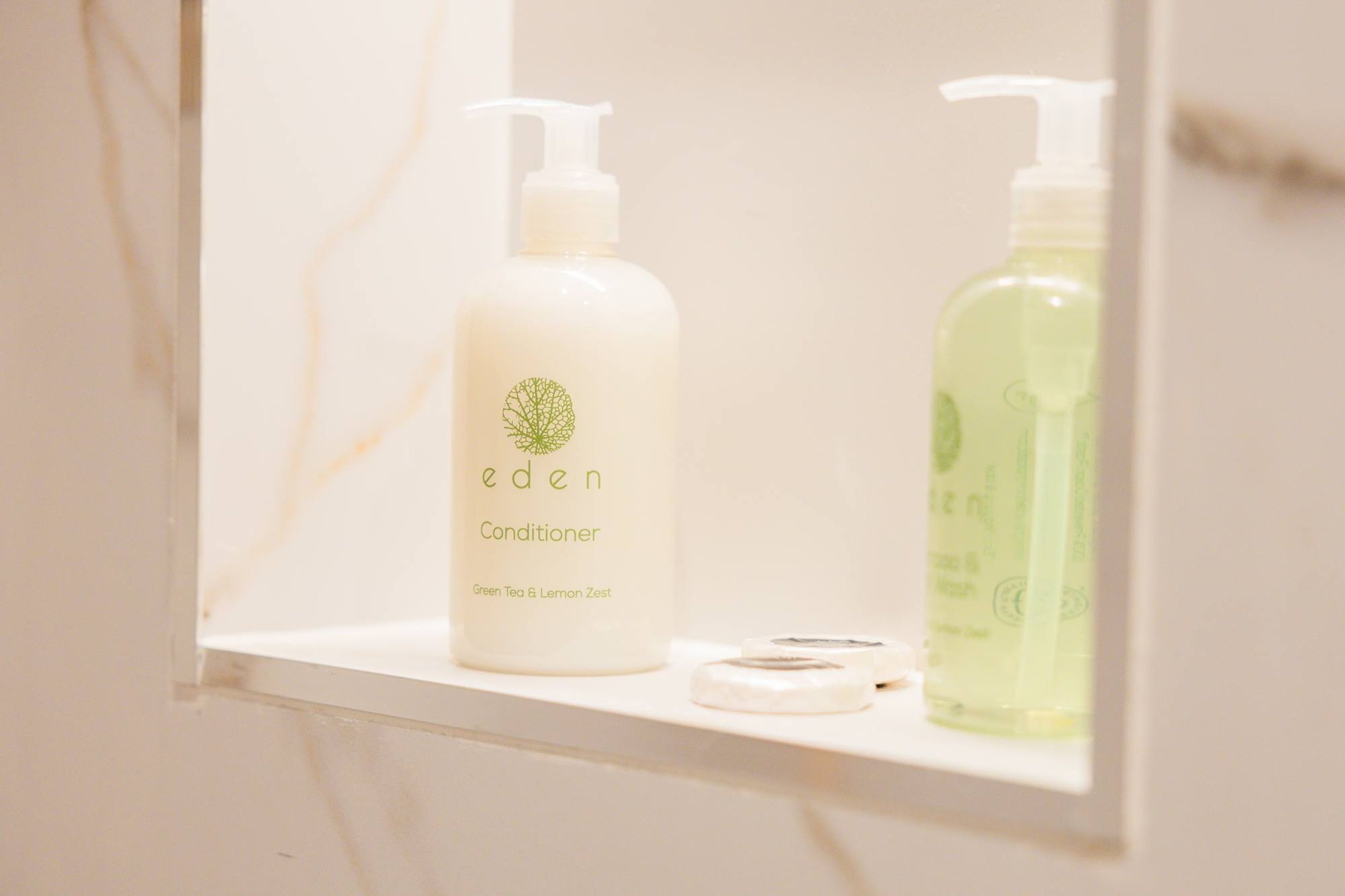 A bathroom shelf with two bottles of Eden conditioner and a soap dish.