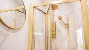 Un bagno moderno con doccia vetrata, pareti in marmo e uno specchio con cornice dorata.