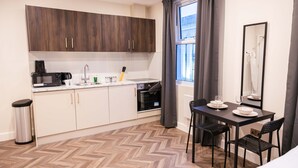 Una cucina compatta con forno a microonde, macchina del caffè e forno. È presente un tavolo da pranzo con sedie e uno specchio.