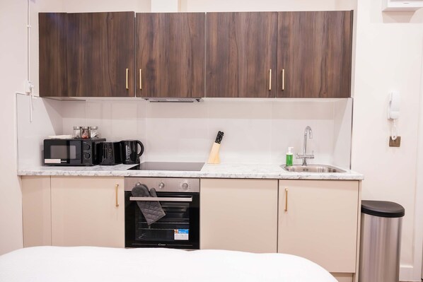A compact kitchen with dark wooden cabinets, a built-in microwave, a coffee maker, and a sink.