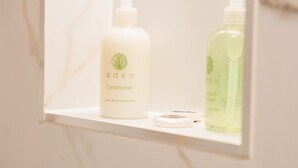 A bathroom shelf with two bottles of Eden conditioner and a small container. - Modern Studio in Central London (London)