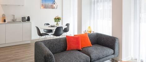 A modern living room with a grey sofa, a wooden coffee table, and a dining area with a white table and black chairs.