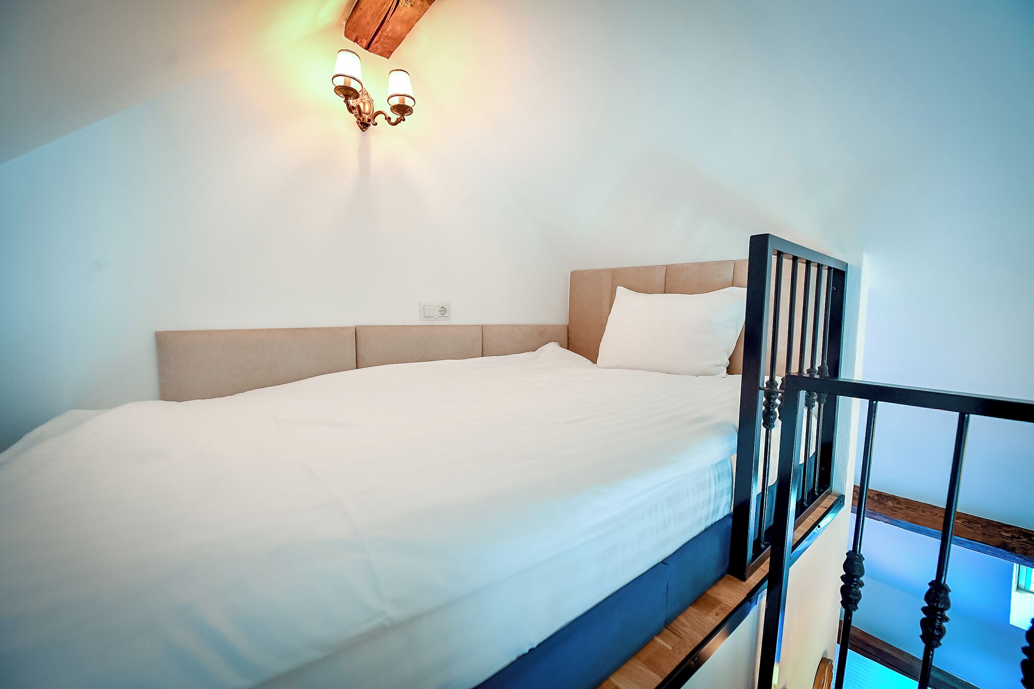 Un dormitorio con una cama, cabecera de madera y una lámpara fijada a la pared.