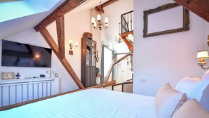 A bedroom with a large bed, a TV mounted on the wall, a wooden ceiling, and a staircase leading to an upper floor. - Casa Barițiu M (Brasov)