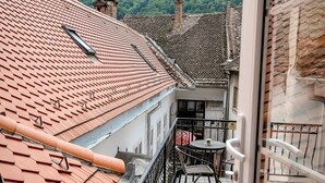 A balcony with a tiled roof, a table with chairs, and a view of a green hill with a tower in the distance. - Casa Barițiu M (Brasov)