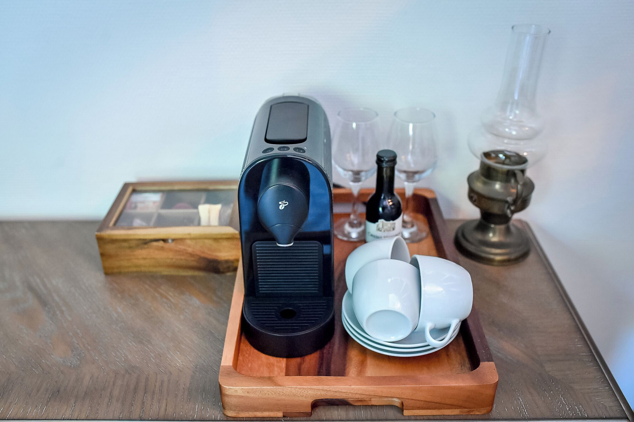 Een koffieapparaat op een houten dienblad met witte bekers en een fles wijn.