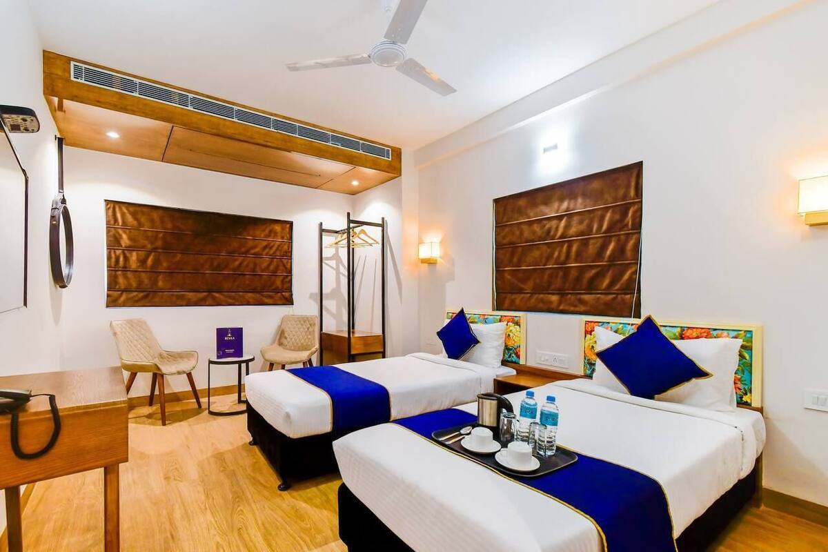 A hotel room with two beds, a desk, a chair, a wardrobe, and a ceiling fan.