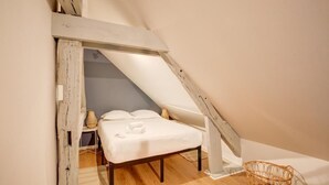 Ein kleines, gemütliches Schlafzimmer mit schrägem Dach, einem Einzelbett, einem Nachttisch und einem gewebten Korb.
