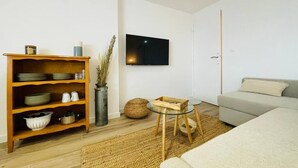 Uma sala de estar moderna com uma estante de madeira, uma TV de tela plana, uma mesa de centro de vidro e um sofá bege.
