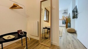 Um corredor com piso de madeira, radiador, espelho, mesa preta com bandeja e um cabide de madeira suspenso.