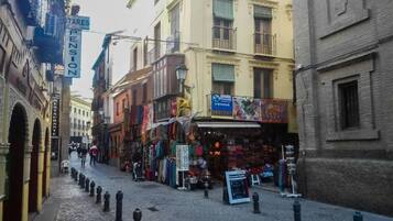 Une rue pavée bordée de boutiques et d’immeubles, où l’on aperçoit une enseigne indiquant la présence d’une pension et une vitrine annonçant une vente.