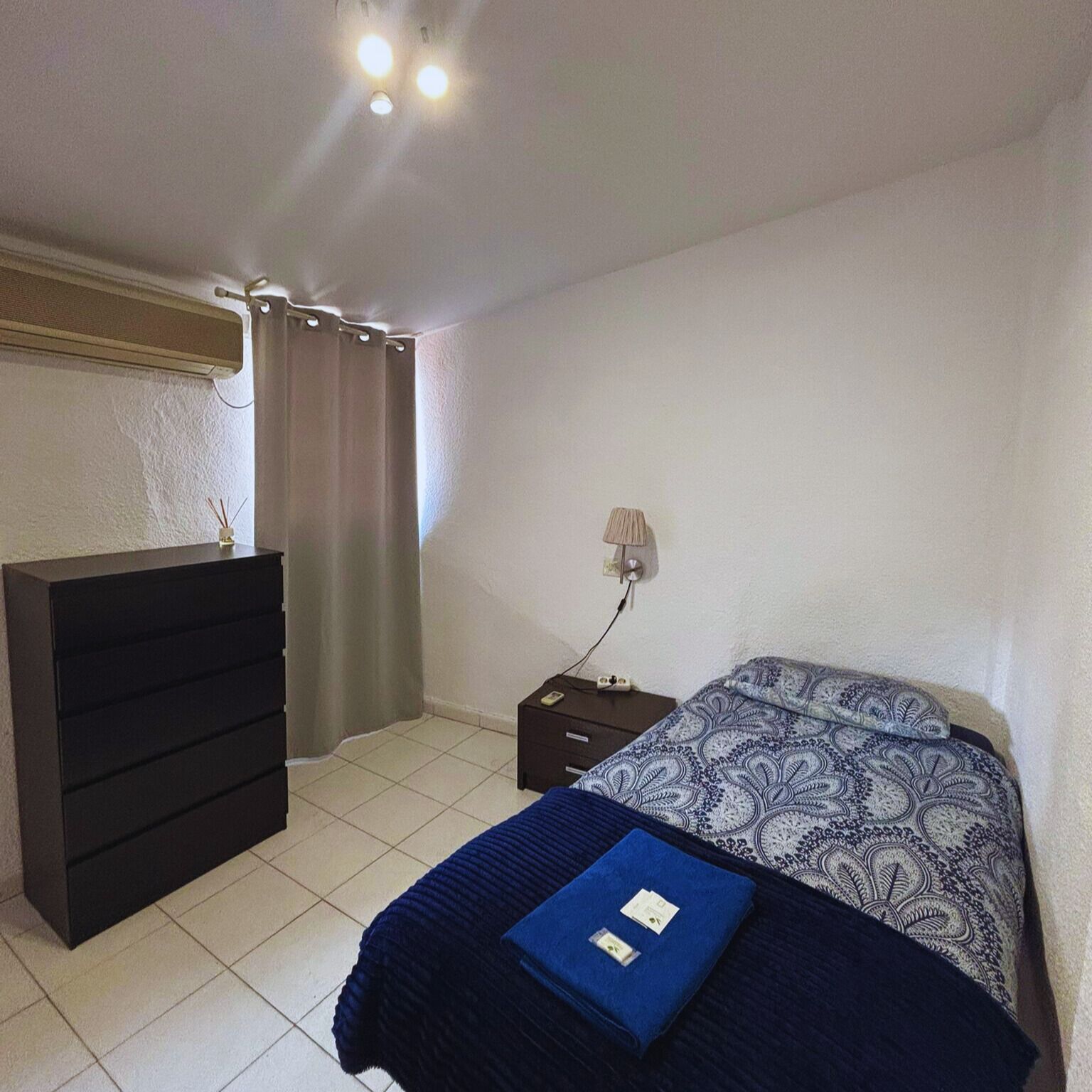 Un dormitorio con cama, cómoda, mesita de noche y lámpara.