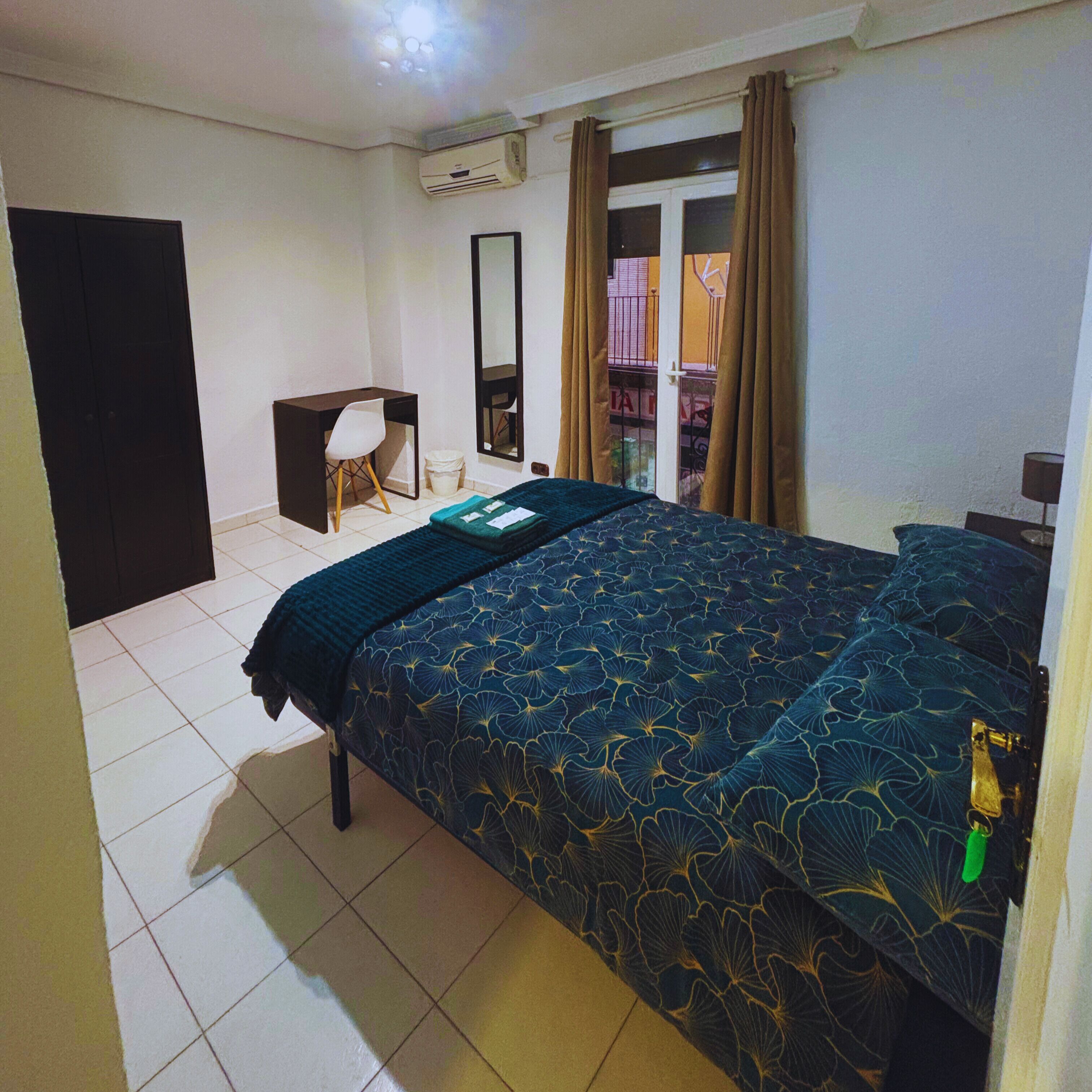 Habitación de hotel con cama, escritorio, silla, espejo y aire acondicionado.