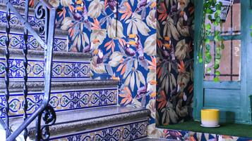 Una escalera con azulejos azules y blancos ornamentados, una barandilla de metal y un muro con diseño de hojas tropicales.