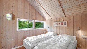 Une chambre avec deux lits, des murs en bois, une fenêtre donnant sur un paysage verdoyant et une étagère avec des photos encadrées.