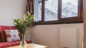 A cozy room with a red sofa, a clear vase with green plants, and a window offering a snowy mountain view.