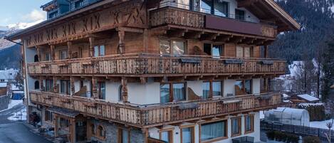 A multi-story wooden chalet with balconies, large windows, and a ski slope in the background.