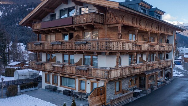A multi-story wooden chalet with balconies, large windows, and a stone facade. - Apartment in Tyrol on the ski-slope (Lermoos)