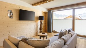 A modern living room with a wooden wall, a flat-screen TV, a round table, and a sofa. - Apartment in Tyrol on the ski-slope (Lermoos)