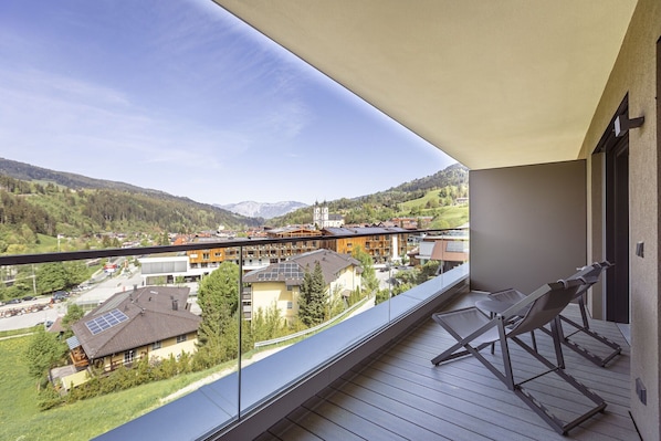 A balcony with a view of a mountainous landscape, wooden flooring, and two lounge chairs.