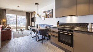 A modern kitchen with a built-in oven, a dining area with a table and chairs, and a large window offering a view of a snowy landscape. - Apartment in Hopfgarten for 4 persons (Hopfgarten)