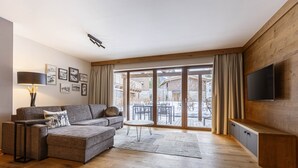 A modern living room with a sofa, a small round table, and a TV mounted on the wall. - Premium apartment with garden (No Deposit) (Ehrwald)