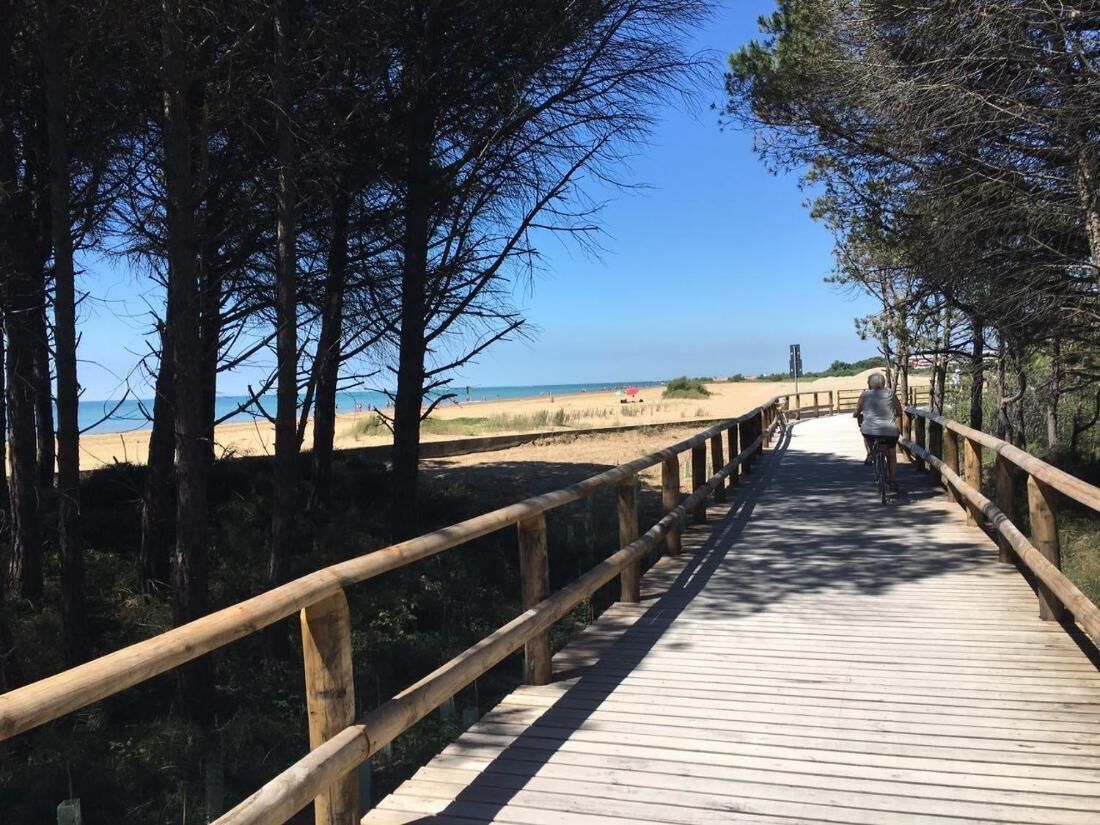 A wooden boardwalk leading to a beach with clear skies and a distant view of the ocean.