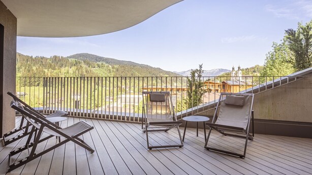 A balcony with wooden flooring, metal railings, and two lounge chairs.