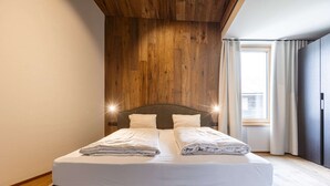 A double bed with white linens, a wooden headboard, and two bedside lamps. - Cosy apartment near ski-slope (Westendorf)