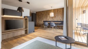 A modern living room with a flat-screen TV, wooden flooring, a dining area with chairs, and a balcony with outdoor seating. - Cosy apartment near ski-slope (Westendorf)