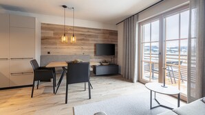 Una sala de estar moderna con comedor, un televisor de pantalla plana montado en una pared de madera y grandes ventanales que ofrecen vistas al exterior.