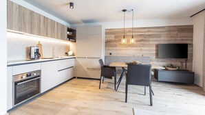 Una cocina moderna con electrodomésticos integrados, un comedor con mesa y sillas, y un televisor de pantalla plana montado en la pared.