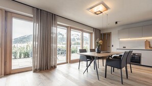 A modern kitchen with a dining area, large windows, and a view of a mountainous landscape. - Beautiful apartment in Tyrol with terrace (Westendorf)