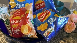 Pöydällä on sininen kulho, jossa on pusseja Walkers-merkkinen juusto- ja sipulimakuinen sekä merisuolalla maustettu uunissa paahdettu sipsi.