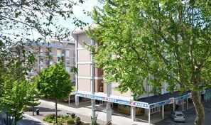 Un edificio de varios pisos con un área exterior techada, posiblemente un estacionamiento o zona de carga, con un letrero que indica 'Mare+' y 'Supermercati'.