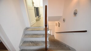Un escalier avec des marches en pierre et une rampe en bois, menant à une pièce dotée d’une porte blanche et offrant une vue sur une salle de bain.