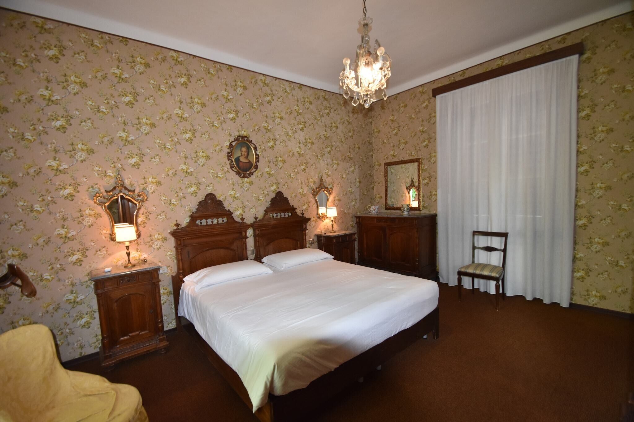 Una camera con un letto grande, due comodini con lampade, una sedia, uno specchio e un lampadario.