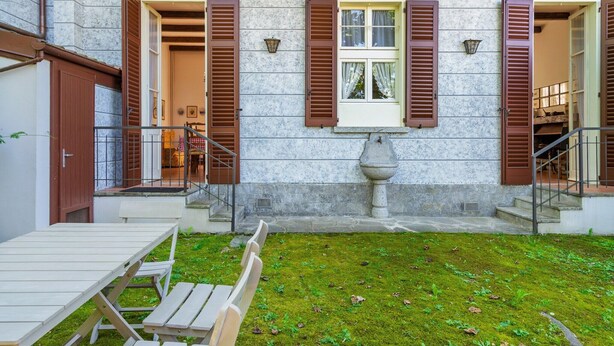 Un bâtiment en pierre avec un petit jardin, des bancs en bois et une table.