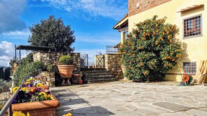 A courtyard with stone flooring, potted flowers, a brick building, and a tree. - Bagno a Ripoli, Italy. Entire accommodation: villa (Toscana)