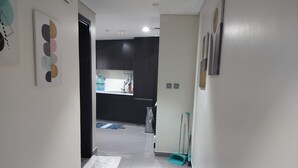 A hallway leading to a kitchen with a water dispenser, a trash bin, and a broom. - 917a Merano -cozy 1 BHK Apartment (Dubai)