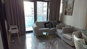 A modern living room with a sofa, armchairs, a glass coffee table, and a small side table. - 917a Merano -cozy 1 BHK Apartment (Dubai)