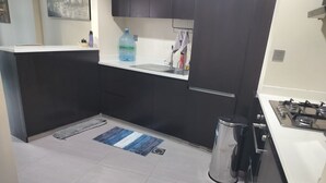 A modern kitchen with dark cabinets, a white countertop, and a stainless steel stove. - 917a Merano -cozy 1 BHK Apartment (Dubai)