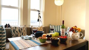 Un coin repas avec une table dressée pour deux personnes, un télescope posé sur le rebord de la fenêtre et une bouteille de vin Norton.