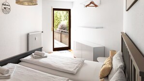 A modern bedroom with two beds, a radiator, a hanging light fixture, and a view of a balcony with greenery. - Vacation apartment Panoramablick in Todtmoos (Todtmoos)