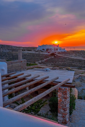 A sunset view from a rooftop terrace with a stone wall and wooden railing. - Villa Ioanna for 10 - Allparos Villas (Paros)